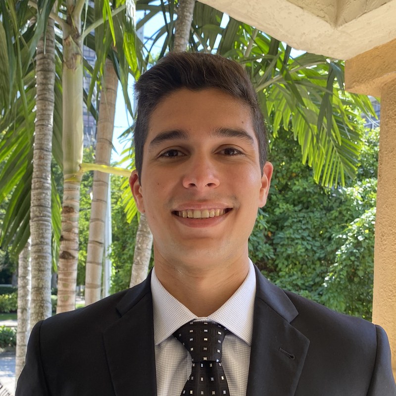 Portrait of Matthew Chavez, MD, in a dark suit with palm trees behind him